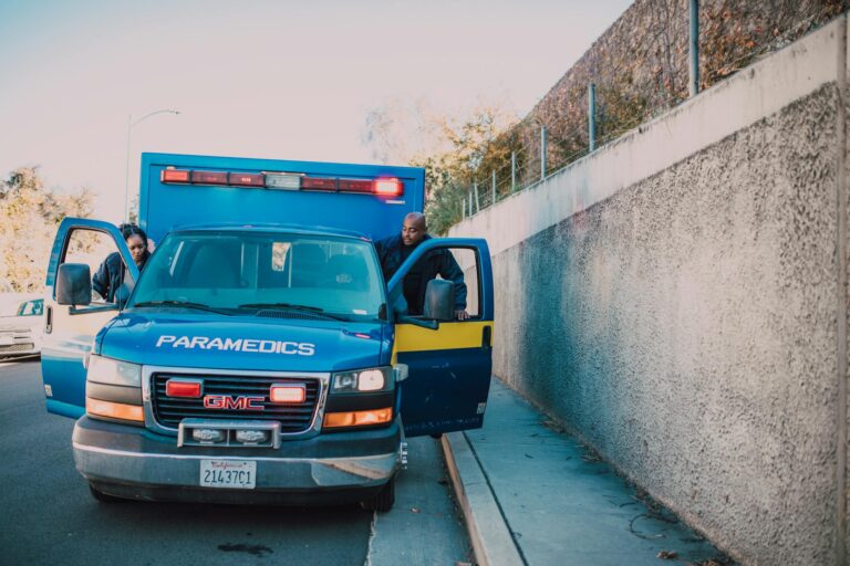 Paramedics attending to an emergency roadside with a visible GMC ambulance.